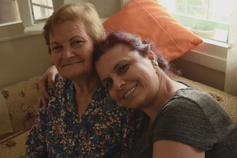 An older woman and her caregiver sharing a warm hug on the sofa