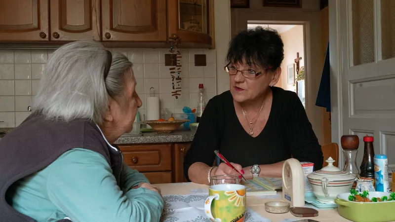 An older woman and her caregiver talking at her kitchen table
